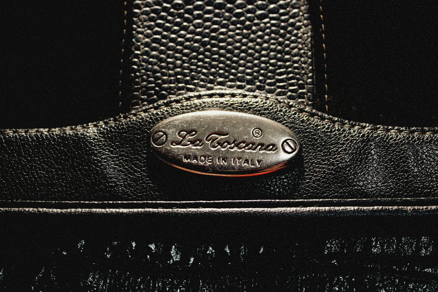 Borsa in pelle nera con targa incisa 'La Toscana MADE IN ITALY'.