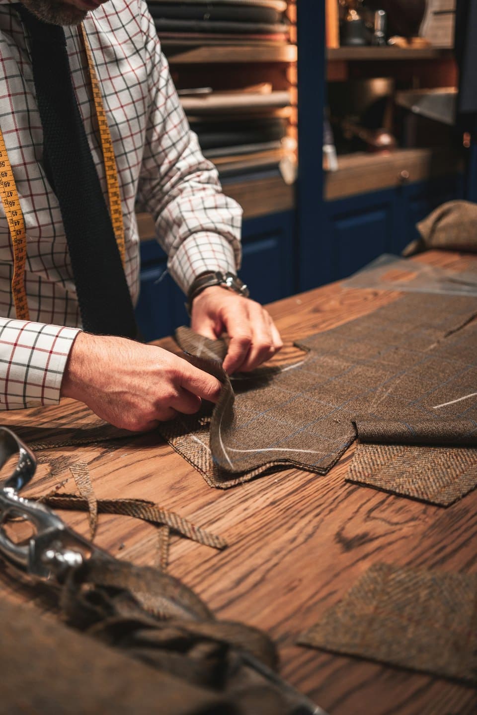 Mani di sarto lavorano tessuto di tweed su un banco da lavoro.